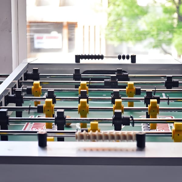 A foosball table with yellow and black players, set against a bright window with green trees outside.