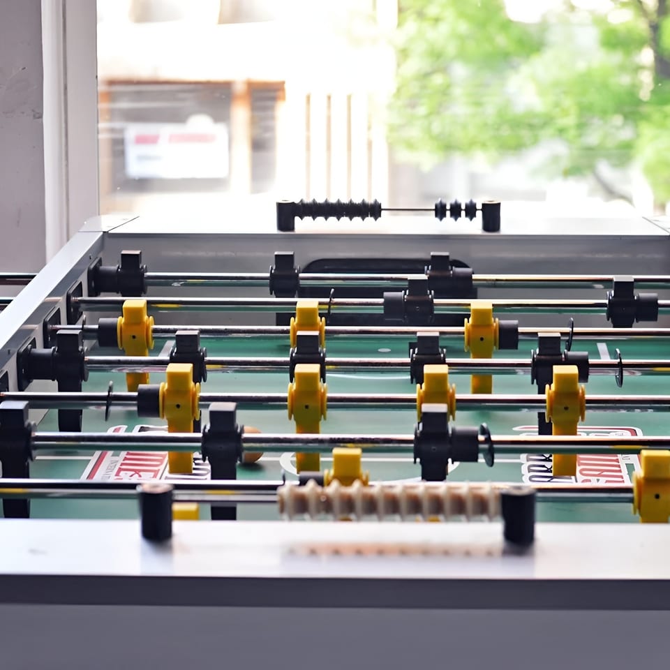 A foosball table with yellow and black players, set against a bright window with green trees outside.
