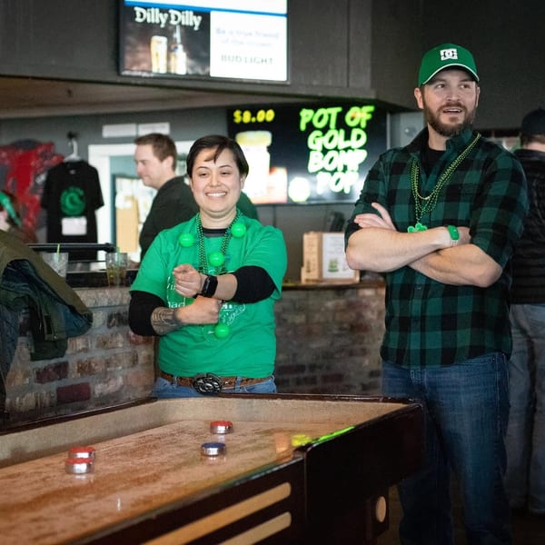 People in green attire playing shuffleboard at a bar with a "Pot of Gold" sign.