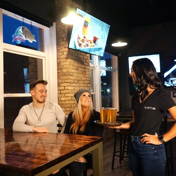 Waitress from The Loft Bar & Grill serves two beers to a couple at a table.