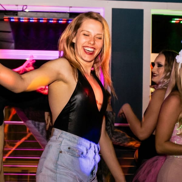 A joyful woman dancing and laughing with friends at a vibrant, neon-lit party.