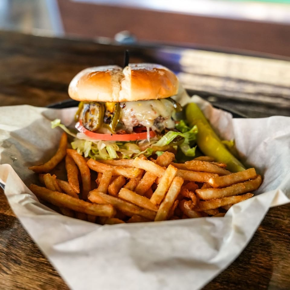 A juicy burger with melted cheese, grilled jalapeños, lettuce, tomato, and a side of fries and pickle.