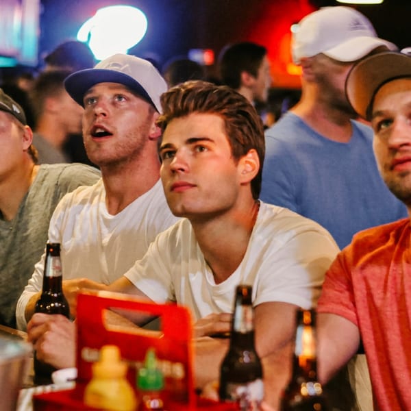 Group of young men watching a screen at a lively bar, with beer bottles on the table.