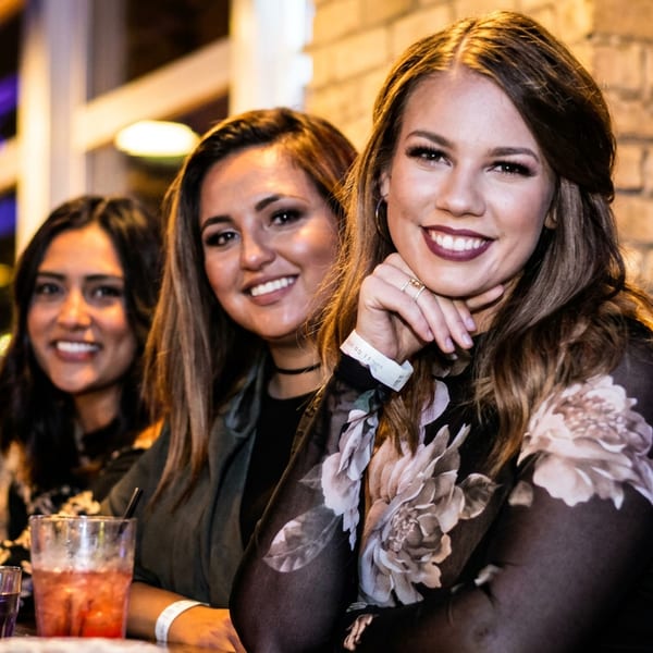 Three smiling women sitting at a bar with drinks.